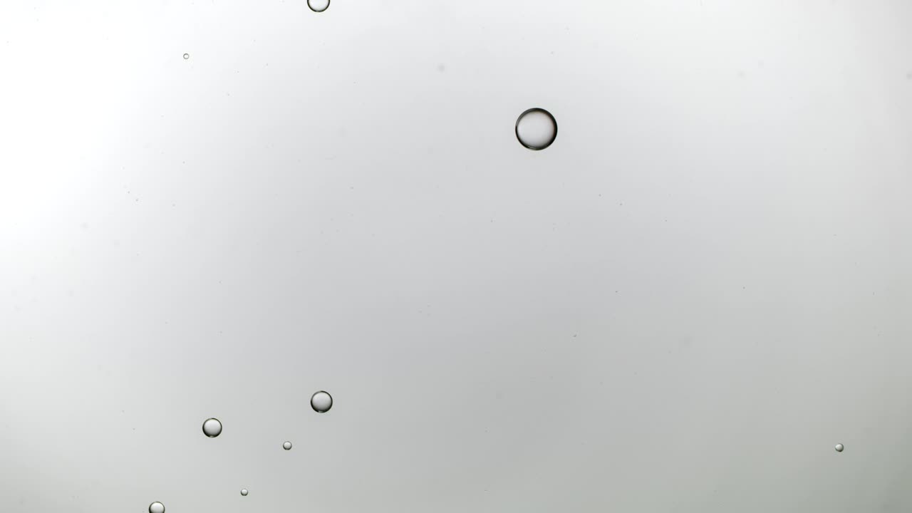 近距离和缓慢运动的头顶视图，倒清楚的油到一个池的水和填补与浮动油滴在一个背光的背景下的框架视频下载