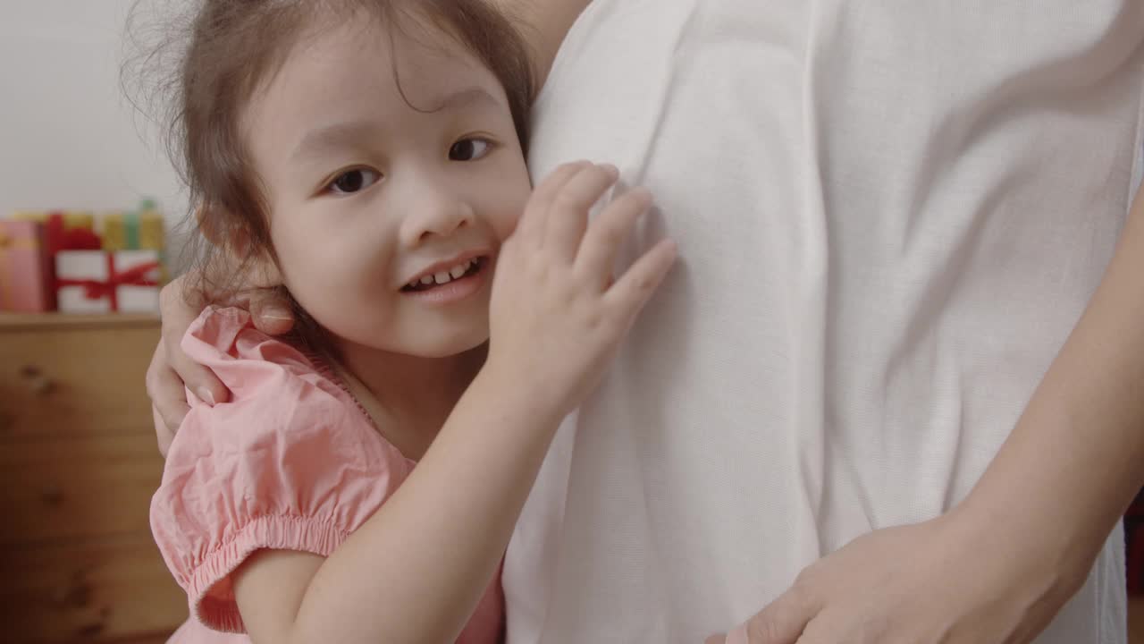 可爱的亚洲小女孩倾听和亲吻孕妇的大肚子。视频素材