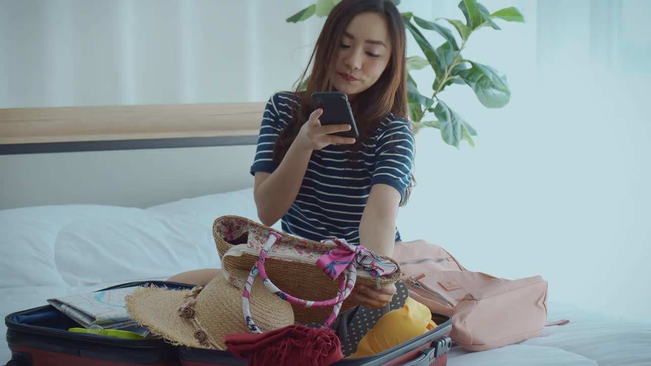 十几岁的女人检查清单，在智能手机上与朋友分享和交谈，打包旅行箱在假期胜利返回旅行。视频素材