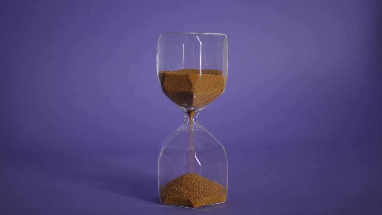 玻璃沙漏与金色的沙子在紫色的背景视频下载