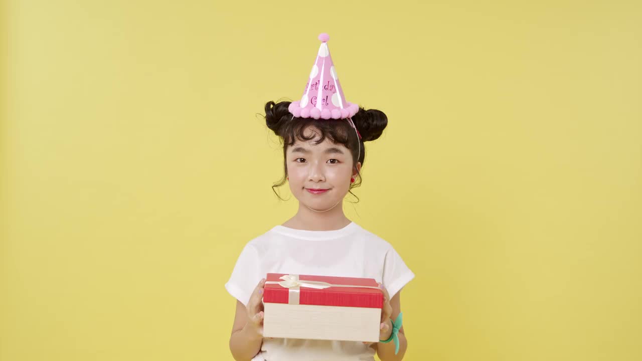 快乐的亚洲小女孩双手捧着礼盒孤立在黄色背景上。视频下载