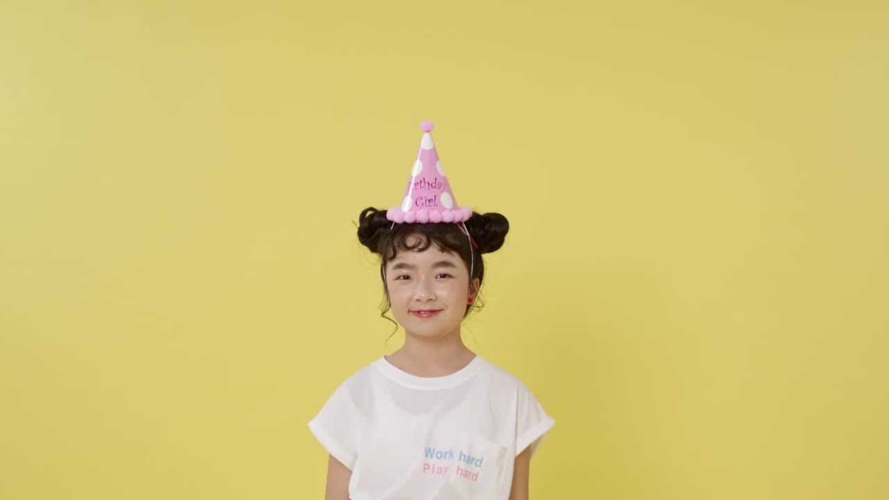 快乐的小女孩庆祝生日。孩子在黄色的背景上跳着彩纸。视频下载