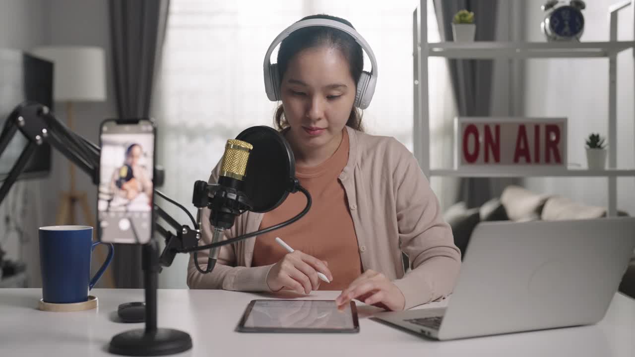 一名年轻的亚洲女子用耳机和麦克风录制播客，看着镜头说话视频素材