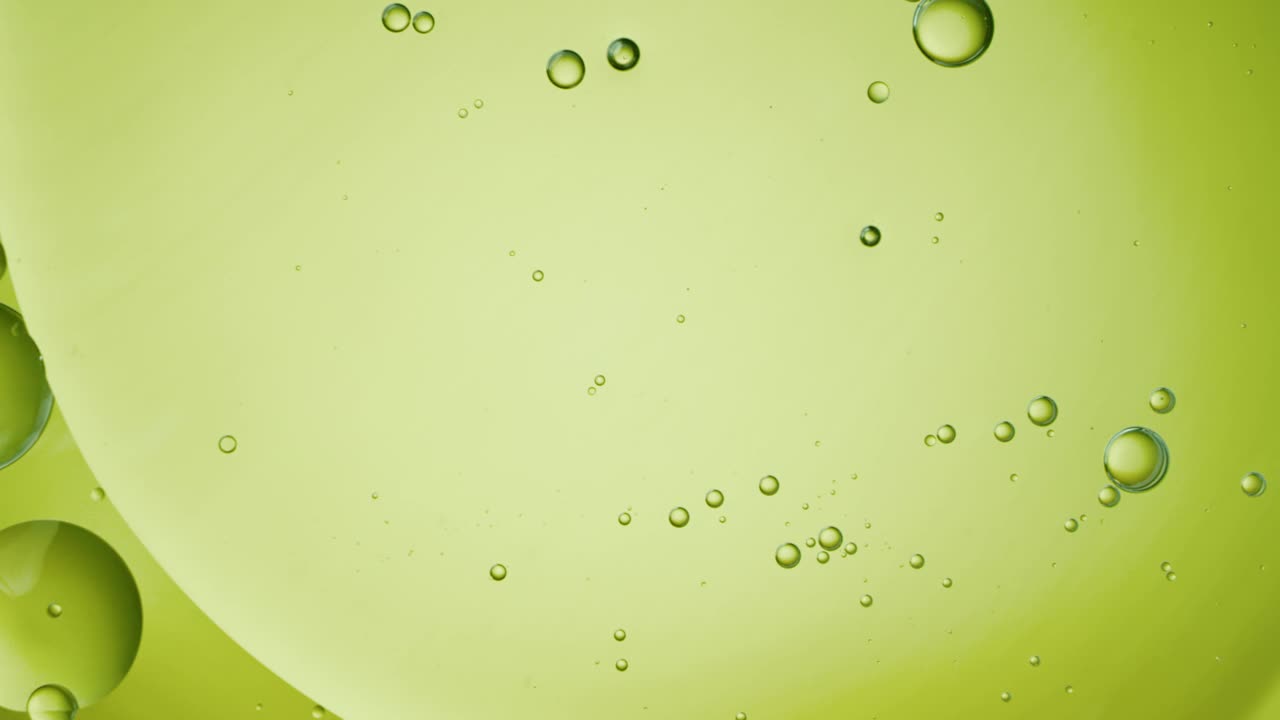 近距离和慢动作的俯瞰视图，将橄榄油倒进一个水池，并在背光背景下用浮动的油滴填充框架。视频下载