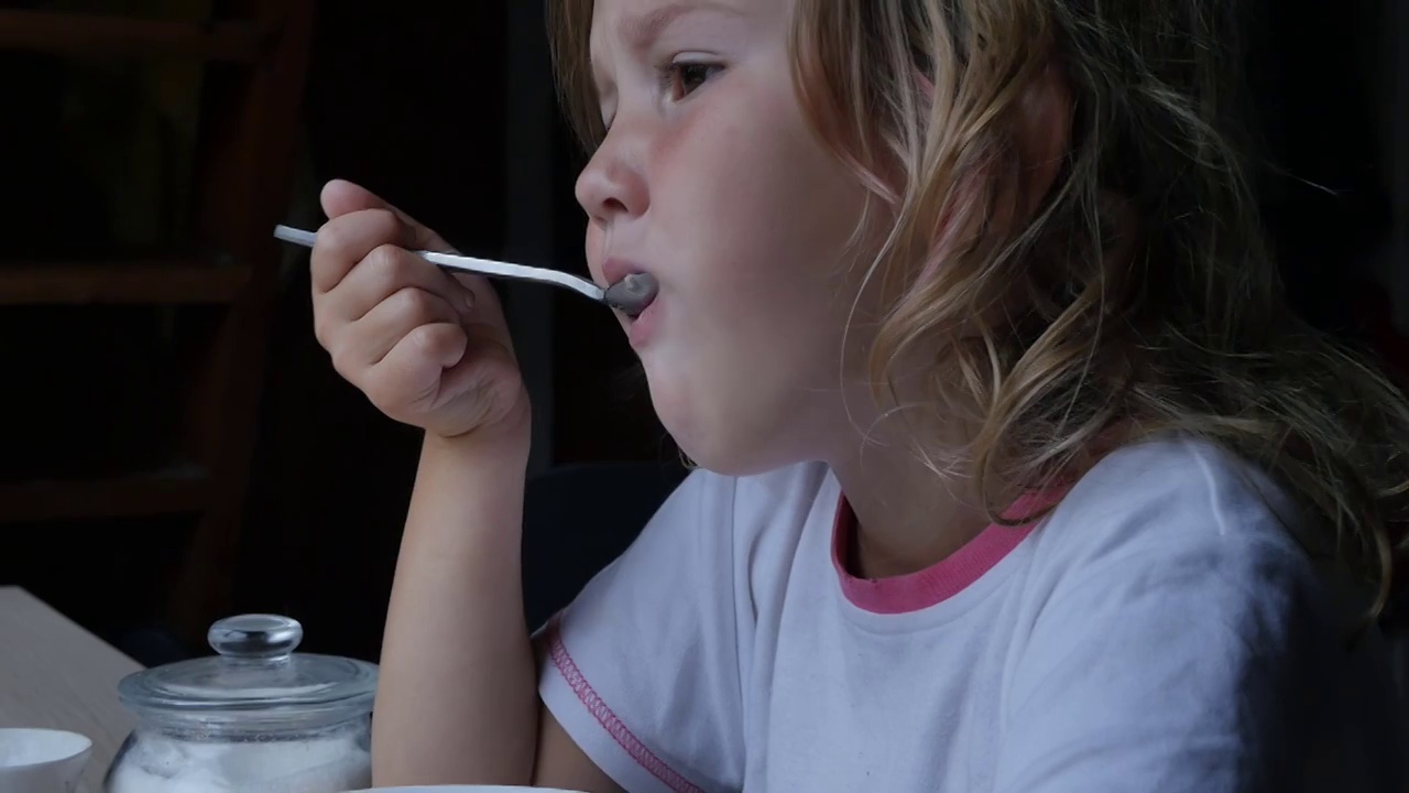 肖像。一个白人少女用大勺子吃燕麦粥。特写,慢动作。儿童健康早餐。视频素材