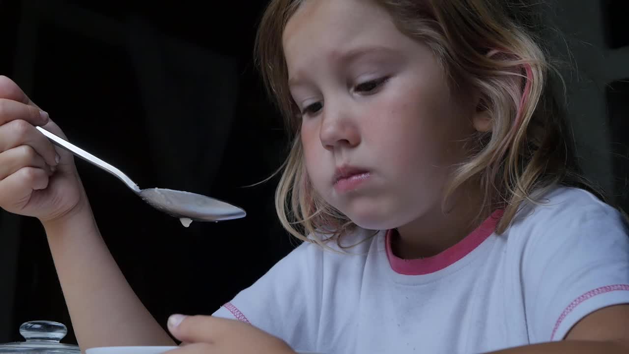 一个可爱的高加索学龄前女孩用勺子吃粥。特写,慢动作。视频素材