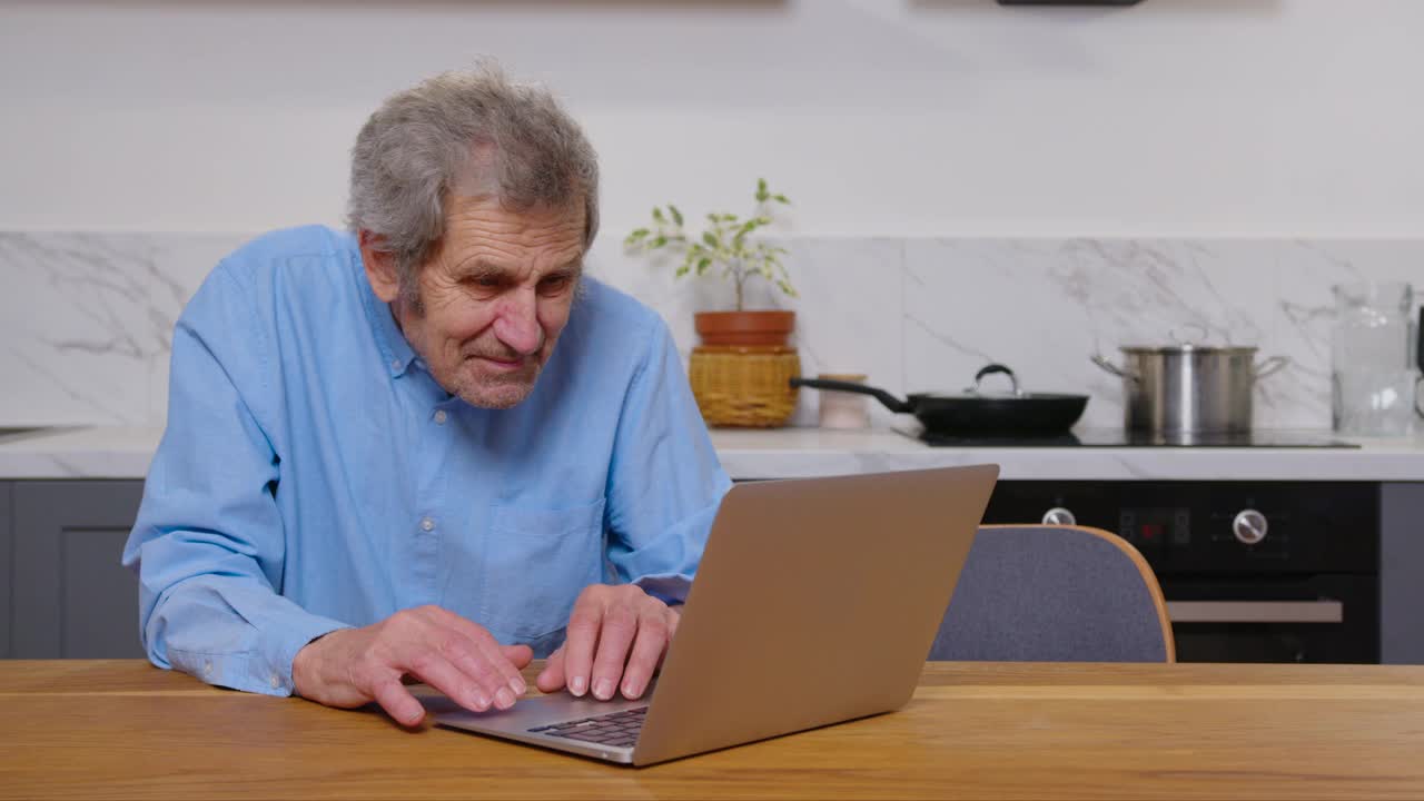 英俊的老人在家里工作的笔记本电脑。收到好消息兴奋而高兴。退休后远程自由工作，老年人积极的现代生活方式。成功的概念。视频素材
