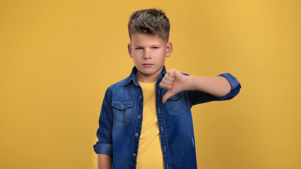 肖像皱眉的男孩做拇指向下的手势不不不摆孤立的橙色视频下载