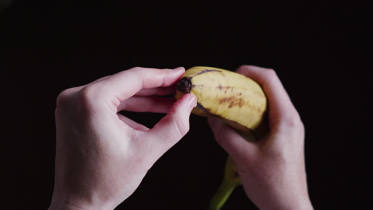 人类的双手正在剥香蕉。在黑色背景下的个人观点视频素材