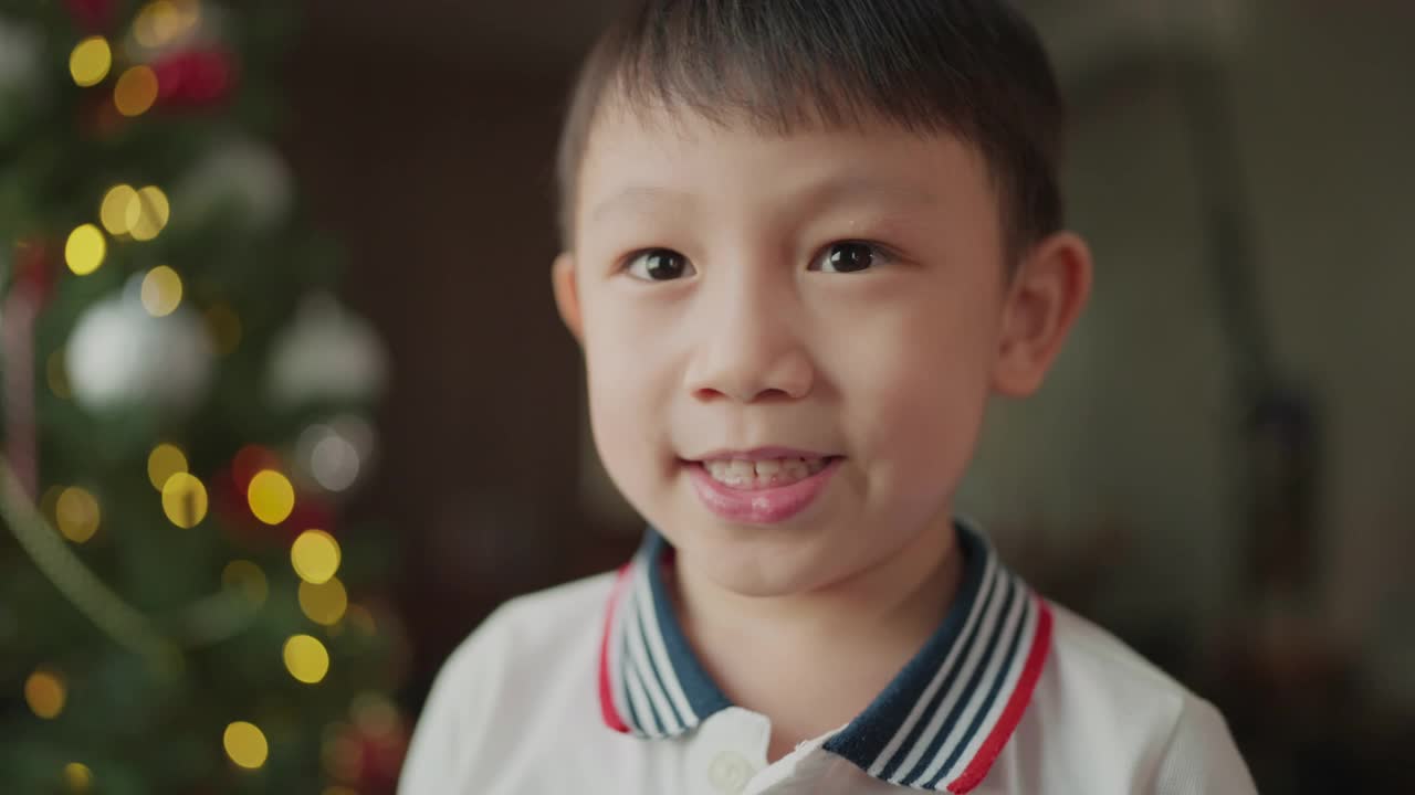 快乐而欢快的亚洲可爱清新的男孩笑着笑着快乐的时刻在圣诞树上装饰着闪亮的球和灯光，亚洲的孩子在客厅里玩着家里的圣诞树，圣诞节假期视频素材