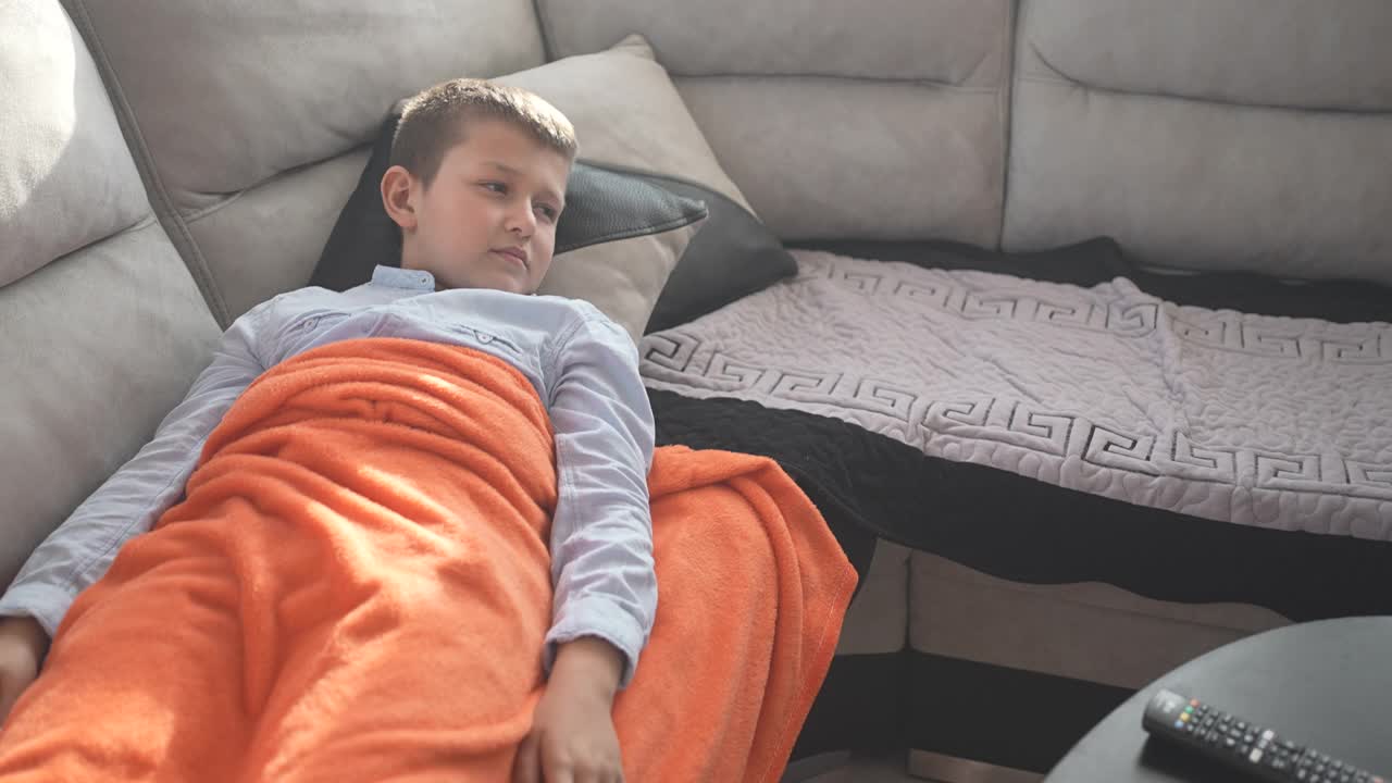 生病的孩子躺在家里的沙发上，一边看电视一边咳嗽视频下载