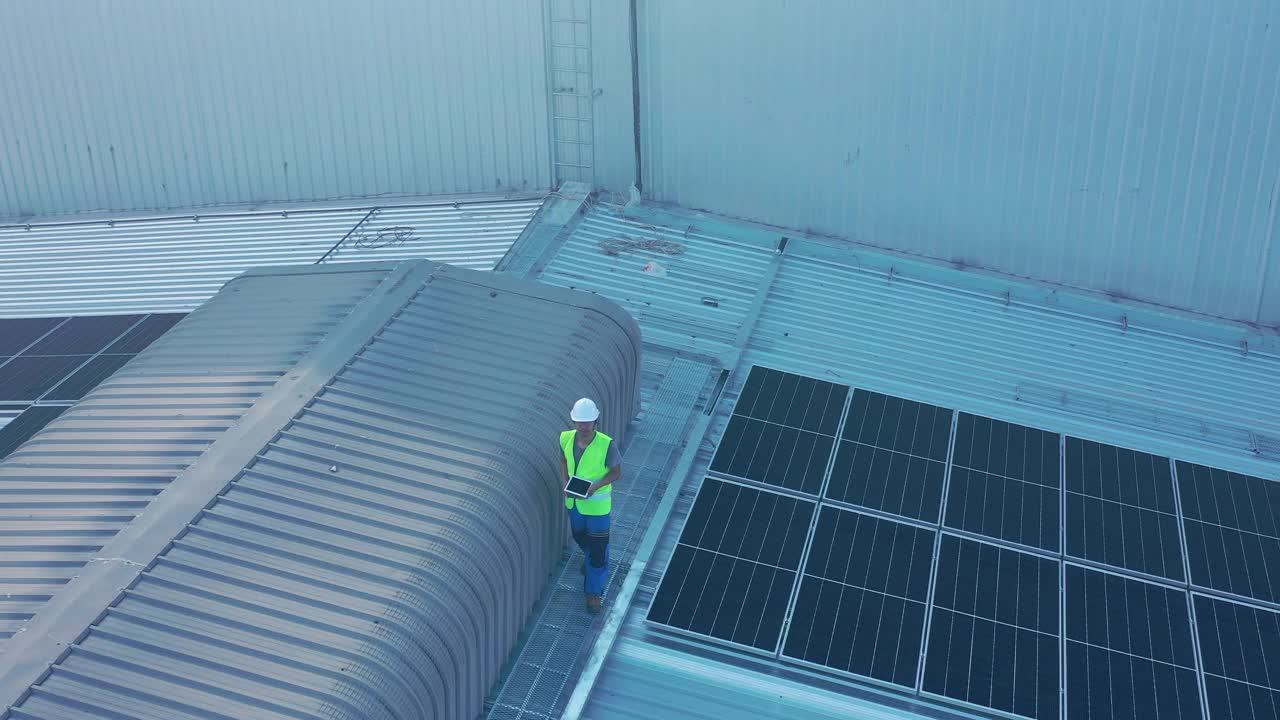太阳能工程师在工厂屋顶行走检查太阳能电池板的鸟瞰图视频下载
