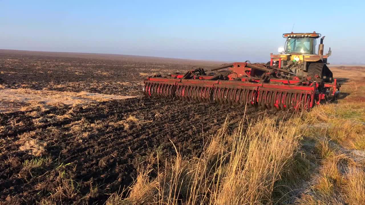 在一个阳光明媚的春日，一台拖拉机在一片大田里犁地。视频下载
