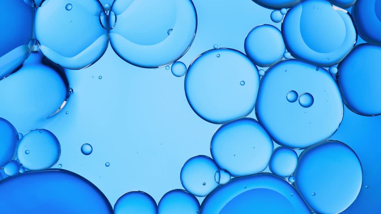 近距离和缓慢移动的头顶视图浮动，流动和爆裂的油滴在水面上的游泳池背光蓝色背景视频素材