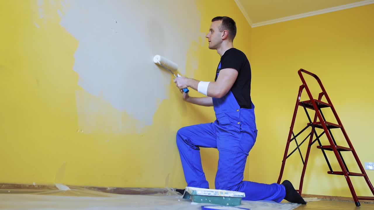 漂亮的工人正在装修墙壁。专业的室内刷、辊装饰油漆工。视频素材