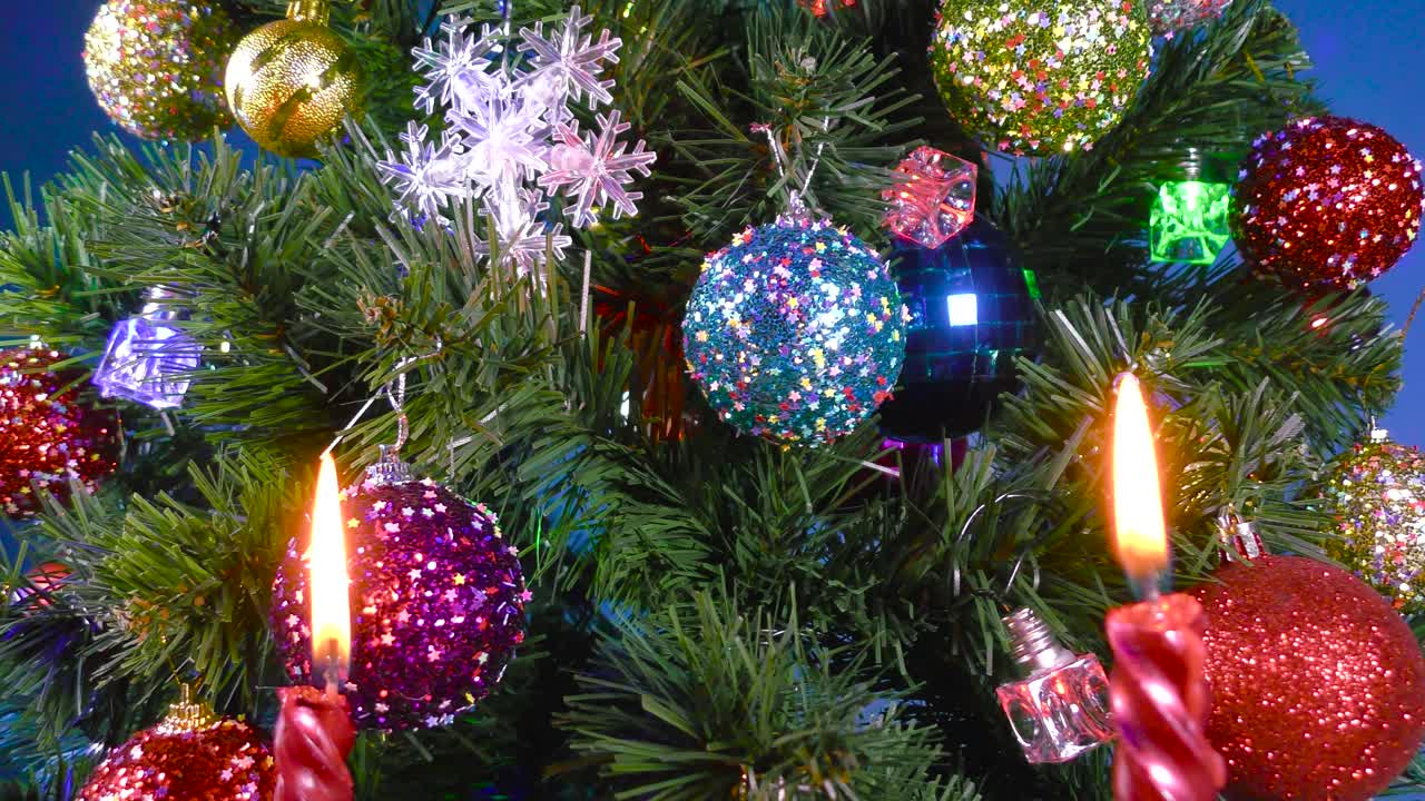 圣诞在燃烧的蜡烛后面的运动特写缓慢旋转的大圣诞树装饰着球和雪花视频下载