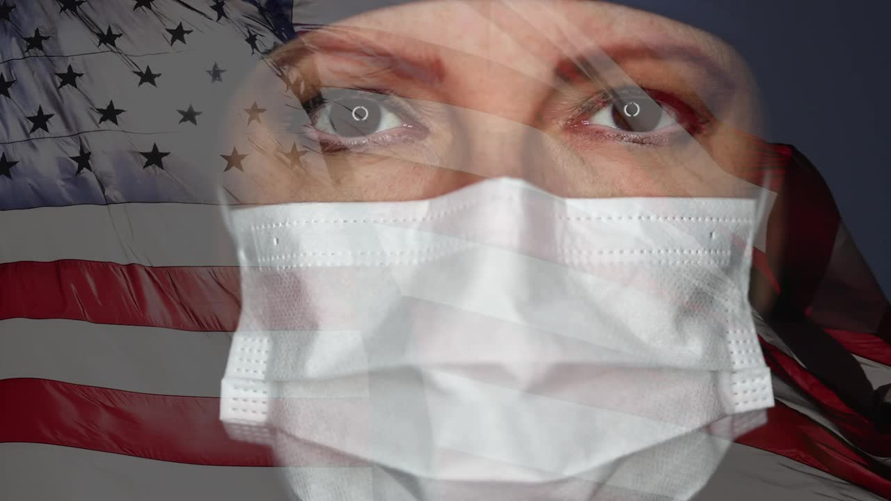 女医生或护士戴着外科医用口罩和帽子，望着摄像机，并以模糊的慢动作挥舞美国国旗。视频下载