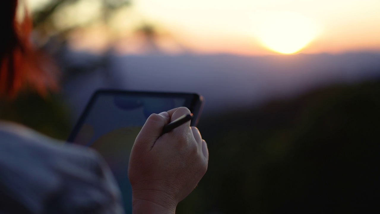 一名女子在夕阳西下的大自然中使用她的平板电脑放松时间视频下载