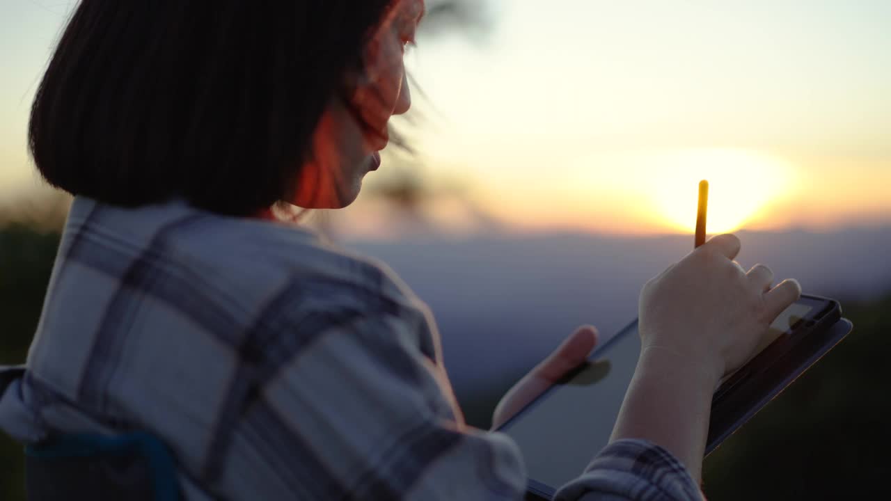 一名女子在夕阳西下的大自然中使用她的平板电脑放松时间视频下载