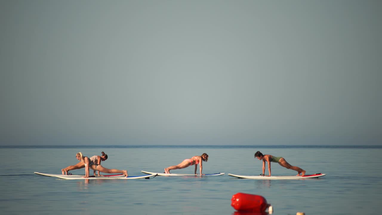 一群穿着泳装的年轻女子在平静的海面上做瑜伽，清晨。平衡姿势-健康生活和身心发展之间的自然平衡的概念视频素材