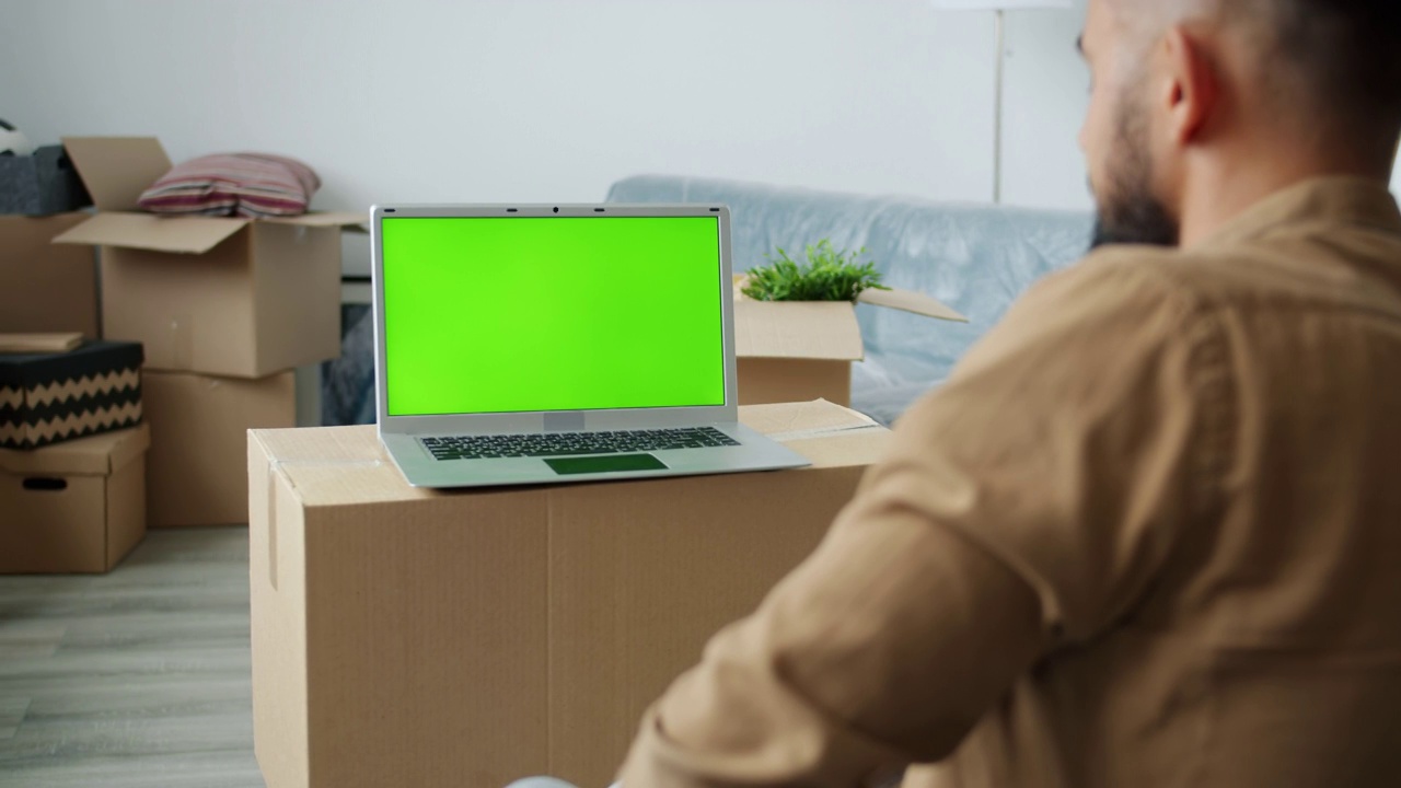 后视图的年轻人看着chroma键绿色笔记本电脑屏幕上的纸箱在新房子视频素材
