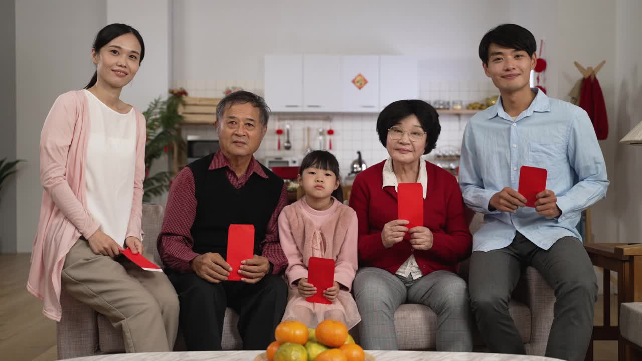 春节期间，幸福的五代家庭在家里拿着红包，对着镜头微笑，用拇指和胜利的手势拍照视频下载