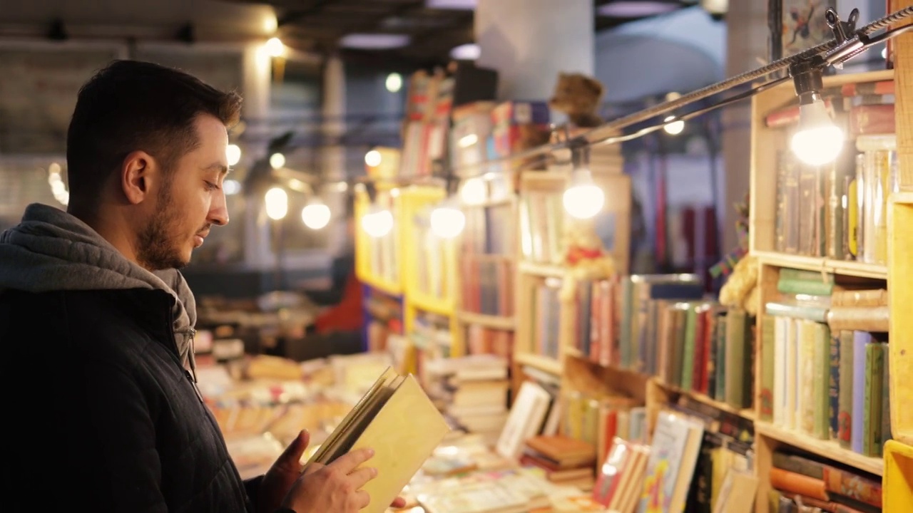 一个年轻人在二手书店里看旧书，在波多贝罗路跳蚤市场的一个市场摊位上出售的旧书视频下载