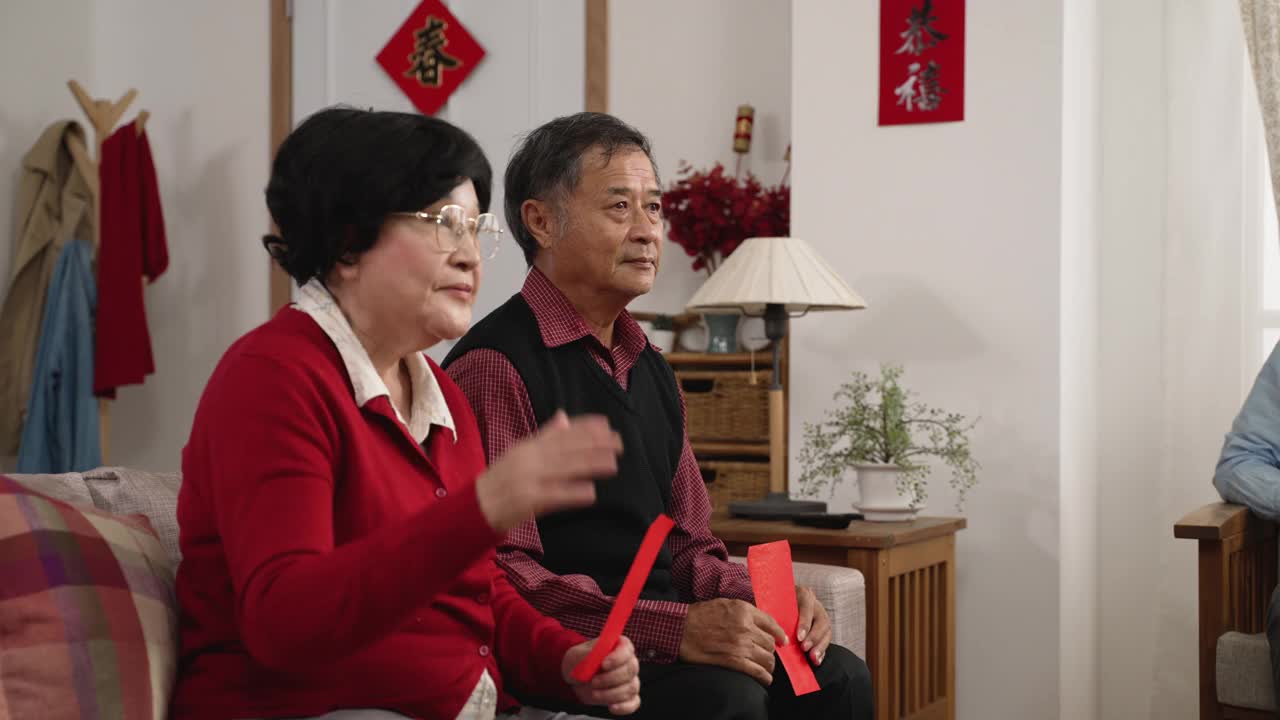 笑容满面的亚洲爷爷和奶奶在中国新年的时候在客厅里向孙女示意要来给她压岁钱。文本翻译:“春天”和“祝贺”视频购买