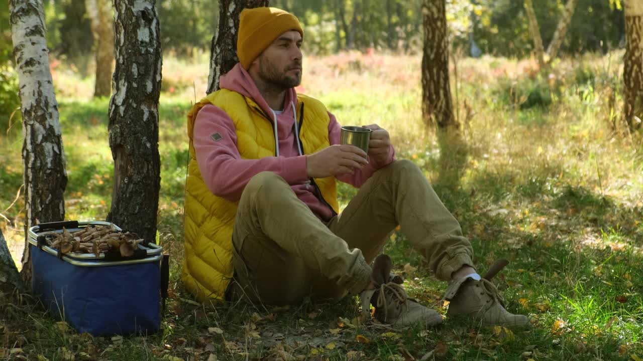 森林里的一个人坐在树桩上喝着热饮。篮子蘑菇视频下载