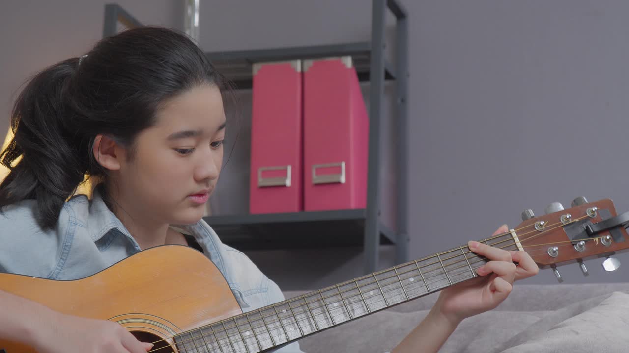 微笑的少女在家里的客厅弹吉他。创造性的爱好视频下载