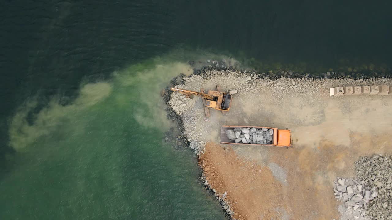航拍视频。从阿博和挖掘机正在建设一个海中的土地。用石头填满岸边。加强海岸线，控制侵蚀，对抗海平面上升。沿海建筑概念。视频下载