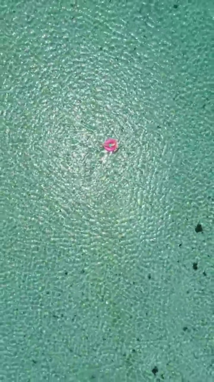 下面是一名年轻女子在热带绿松石原始海滩上放松的鸟瞰图。视频素材