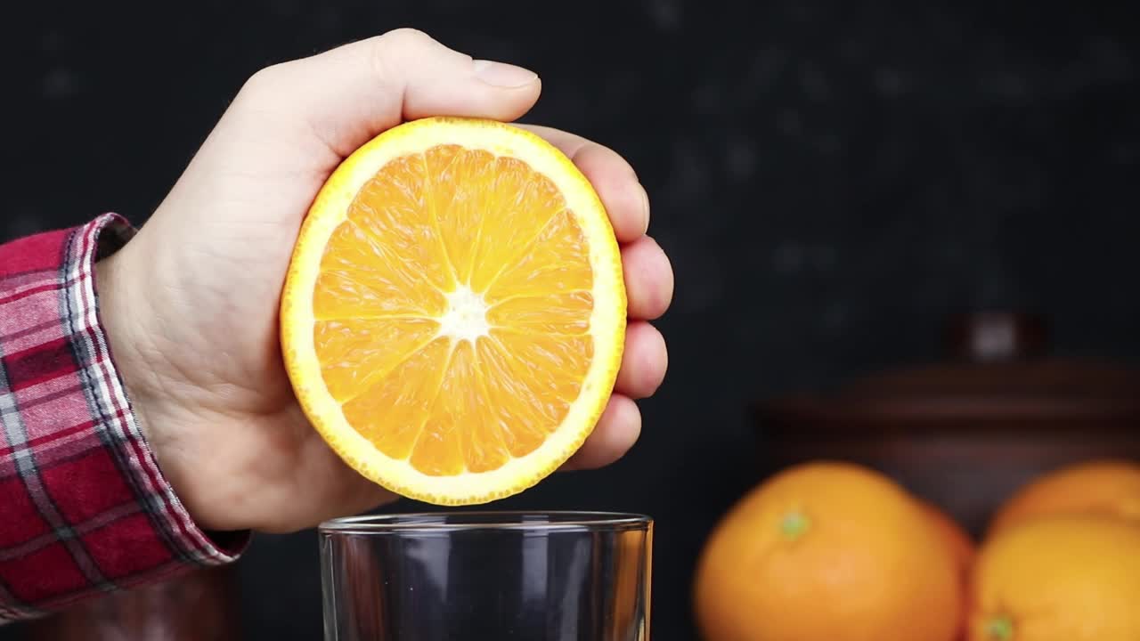 一个男人把橘子汁挤到杯子里。新鲜的橙汁。健康的素食。维生素的食物。成熟的橘子。视频素材