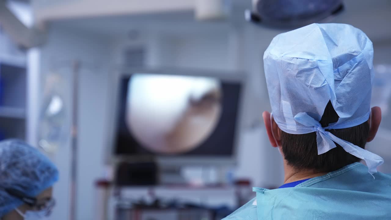 医生们在手术室里使用现代化的医疗设备。外科医生进行手术，并在监视器的屏幕上观察整个过程。后面的观点。视频素材