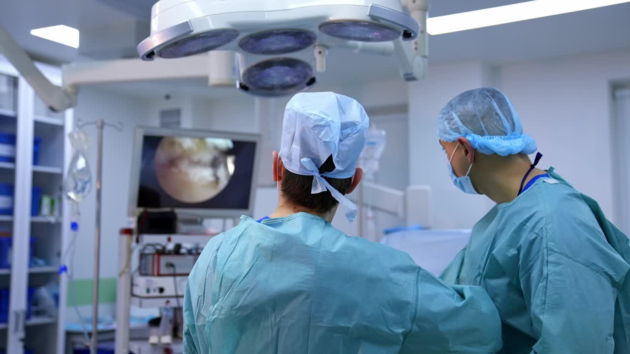 医生在屏幕上观察手术。在现代医院里，身穿医疗制服的专业外科医生看着显示器进行手术。视频素材
