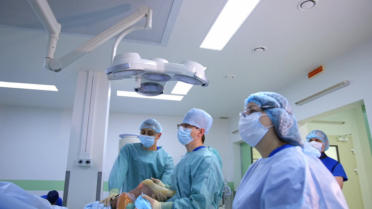 外科医生的联合工作。在现代医疗室背景下，一群医生在给病人做手术时直视着病人。卫生保健的概念。视频素材