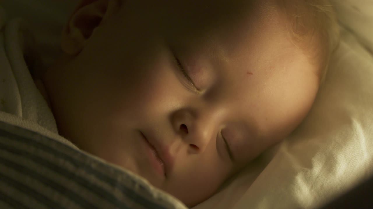 婴儿襁褓躺在婴儿床，9个月的男婴睡在夜灯下。9个月大的白人小孩的脸特写。视频下载