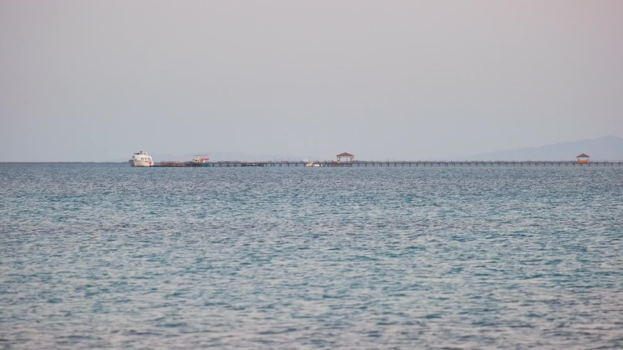 海景与波浪表面的蓝色海水与遥远的船在长码头的尽头漂浮在平静的波浪视频素材