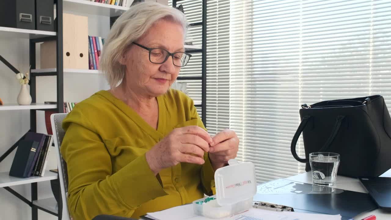 一位老年妇女在家从日常药盒中服用药物。视频下载