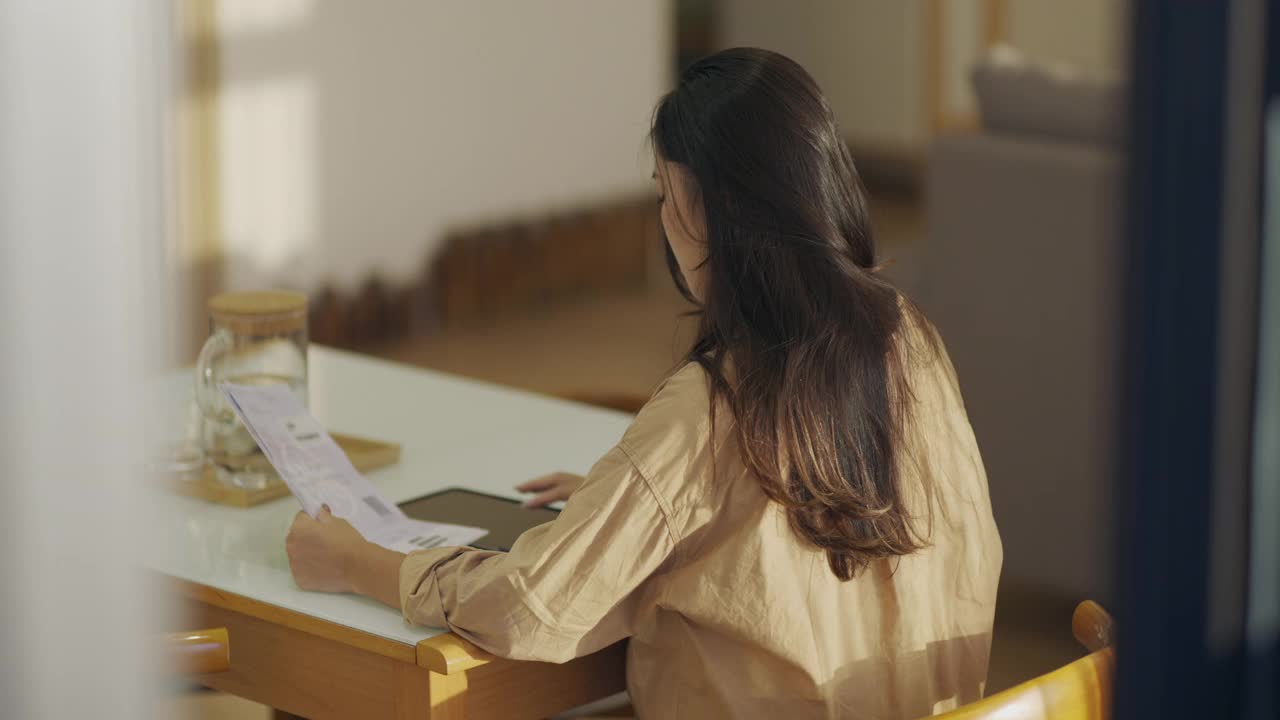 年轻的亚洲妇女在家里的桌子上用计算器计算财务家庭，检查账单，为家庭节省开支成功视频下载