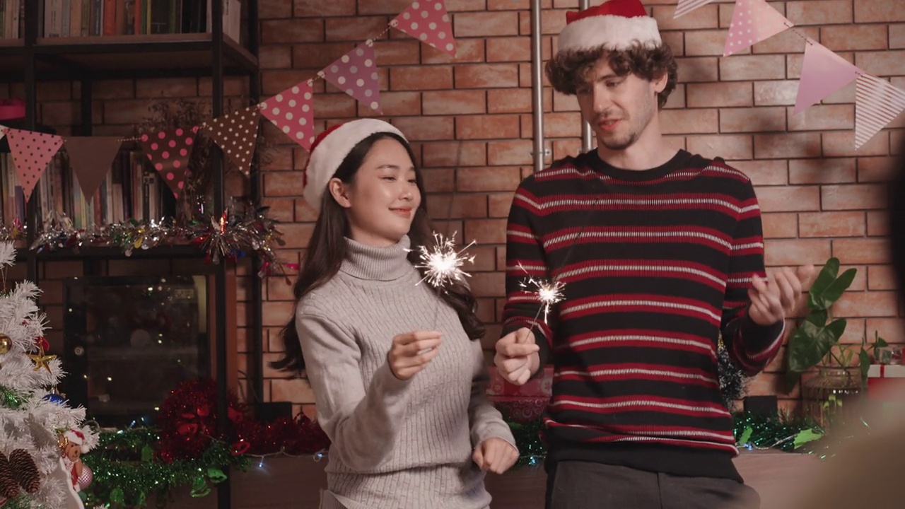 欢乐的年轻亚洲妇女和美国男子在庆祝圣诞晚会上，一边欣赏烟花，一边跳舞视频素材
