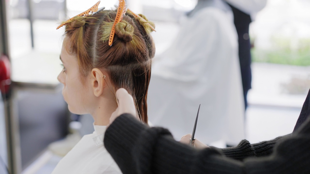 侧视图:美发师在美发厅用剪刀和梳子为一位棕金色头发的年轻女子剪时髦的发型。视频素材