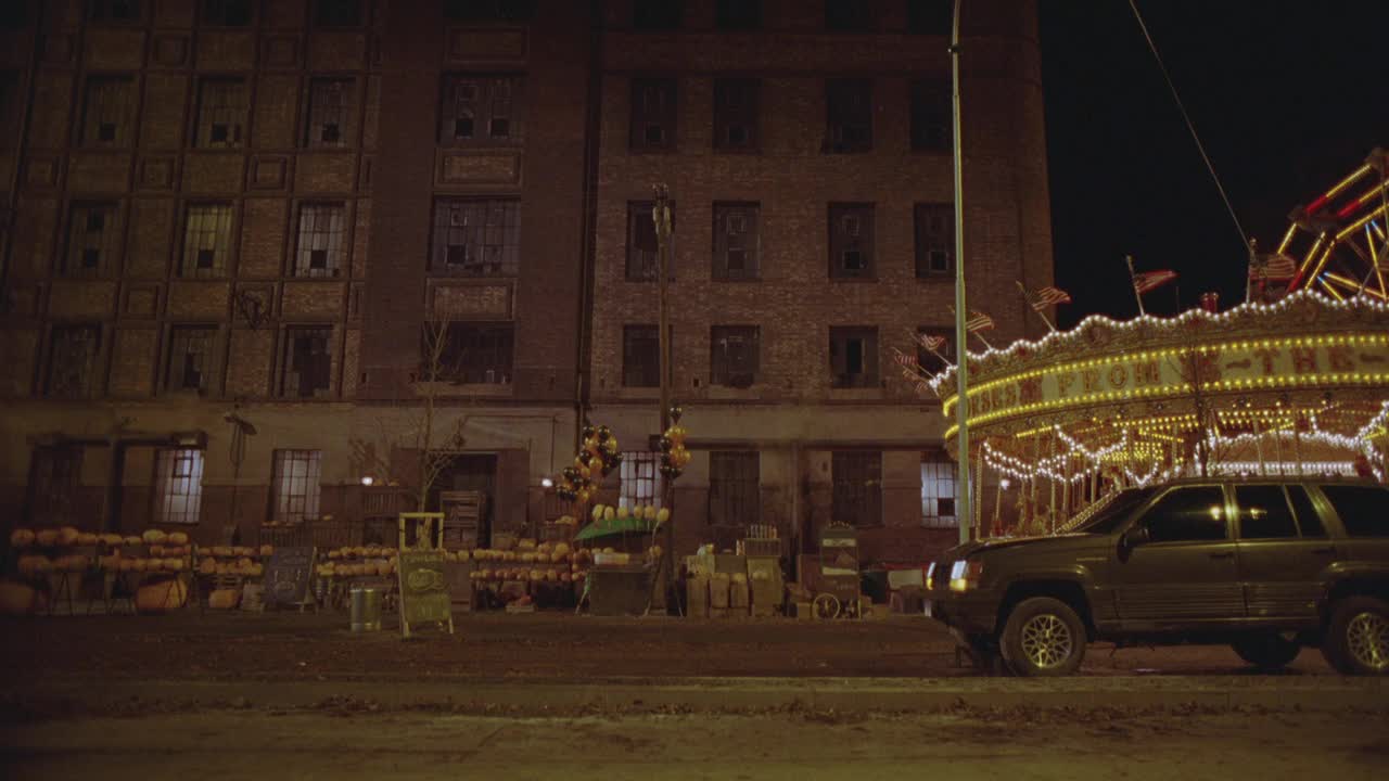 广角1993吉普大切诺基越野车翻转360度，一头撞到街上。旋转木马与灯光和美国国旗附近的南瓜站和多层废弃建筑破碎玻璃的窗户在bg。视频下载