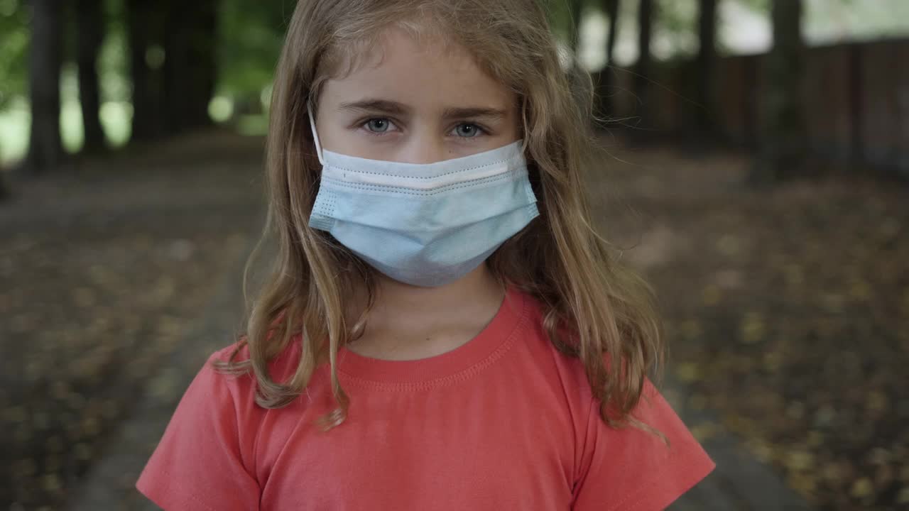 流行，小女孩在城市街道上戴着防护面具的肖像。儿童戴口罩保护自己免受病毒空气污染。冠状病毒流行Covid-19。流感冠状病毒。视频素材
