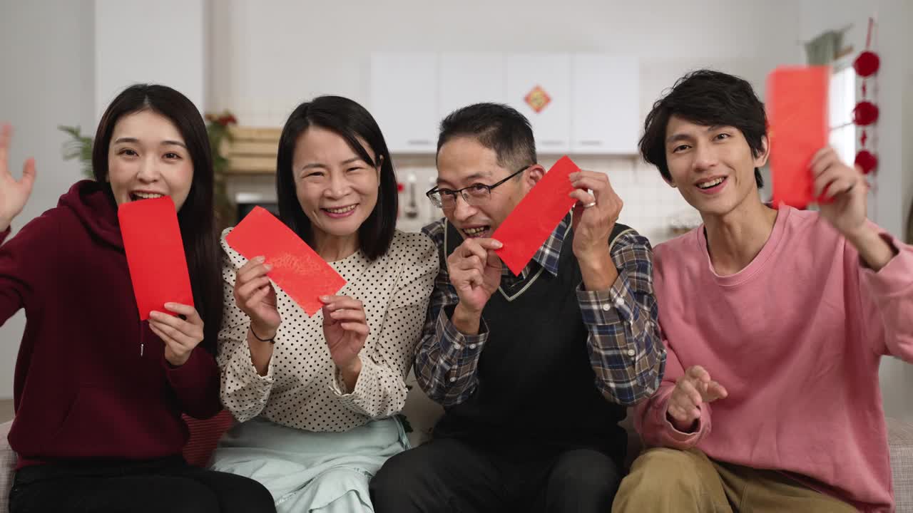 快乐的亚洲父亲，母亲，女儿和儿子在镜头前微笑，炫耀他们手中的红包，并与朋友在中国新年视频电话视频下载