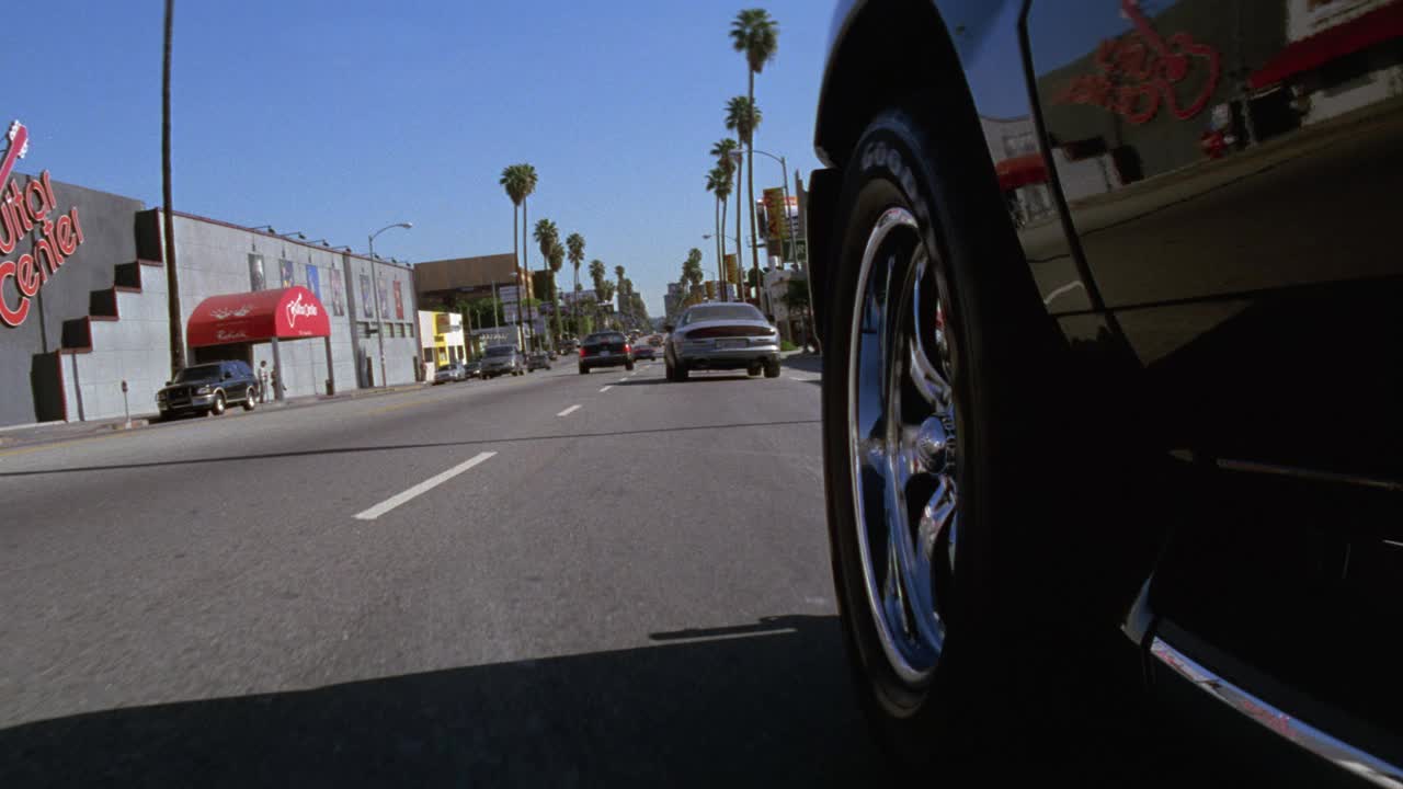 广角移动pov 3/4直向前左后轮胎保险杠在城市街道上超速行驶的汽车的pov。路过棕榈树和吉他中心的“音乐店”。可能是追车。日落大街,好莱坞。视频素材