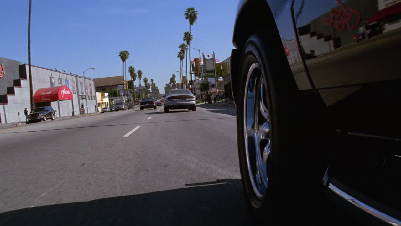 广角移动pov 3/4直线前进左后轮胎保险杠在城市街道上急转弯和超速行驶的汽车的pov。路过棕榈树、车辆、红绿灯、广告牌和商店。可能是追车。日落大街,好莱坞。视频素材
