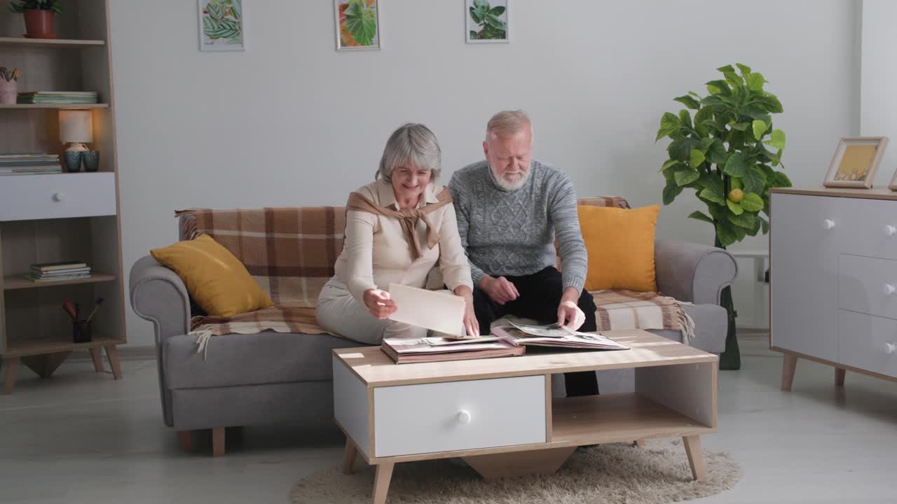 老人们一家人一起坐在沙发上，拿着古董相册，祖父母们一边享受着回忆，一边用照片讨论着愉快的时刻视频下载