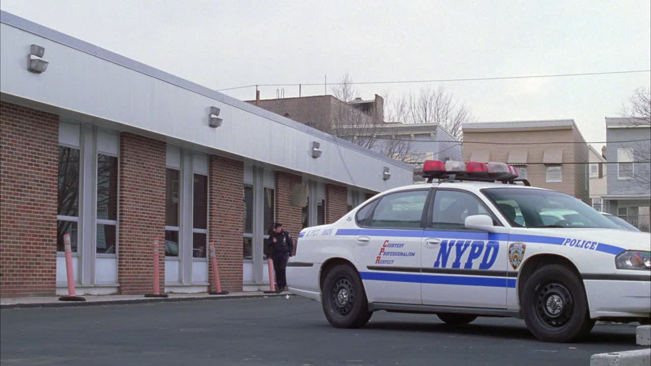 广角低二男警官或男子沿着一层砖楼或警察分局走。警察停车场，可以看到纽约警察局的警车。背景是两层和多层的公寓楼。BIZBARS。视频素材