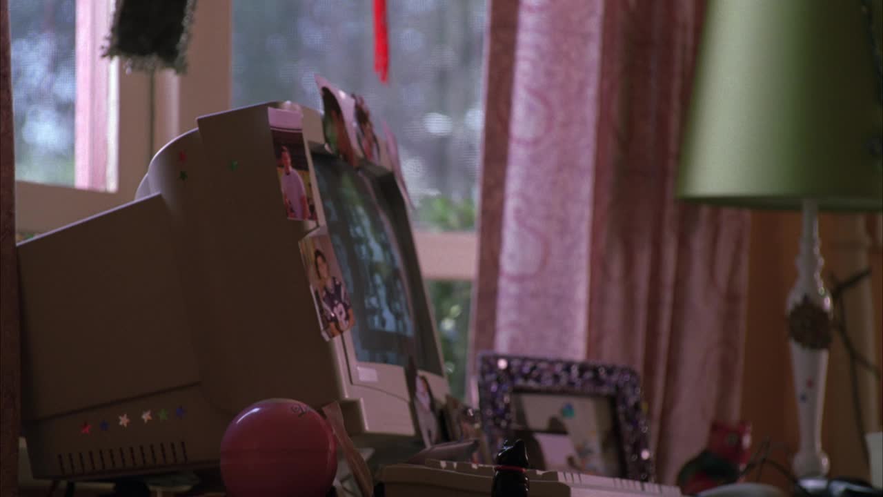 中角度的电脑和键盘，装饰着贴纸和人的照片，靠近灯和打开的窗户。桌子上有猫雕像和魔法八球。可能是少女的卧室。视频下载